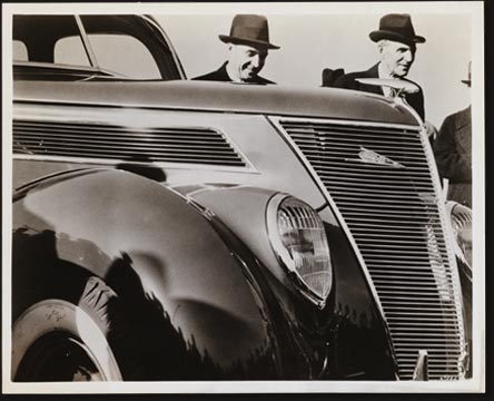 This unusual camera shot shows Henry Ford (right) and Edsel Ford with their newest product, the Ford V-8 for 1937. The picture was taken at Dearborn during the newspapermen’s preview of the new car, which excited unusual interest because of its completely new appearance and the advent of the 60 horsepower V-8 engine, giving a choice of engine sizes.