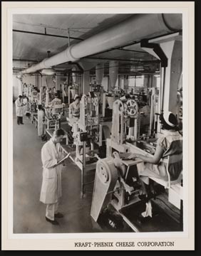 A view in the packaging room in one of the many Kraft plants throughout the United States. Immediately after pasteurization, these ingenious machines foil-wrap and seal the cheese in air-tight, dust-proof, sanitary packages to protect its purity and freshness. The operation is automatic from beginning to end. This battery packages over 200,000 half-pound units daily.