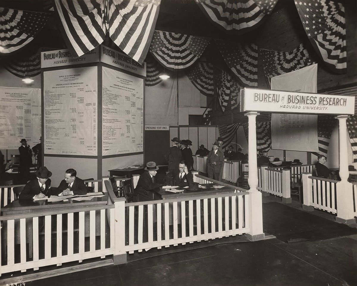 Black and white photograph of men gathered in groups talking in Harvard’s Bureau of Business Research booth at the Chicago Shoe Convention.