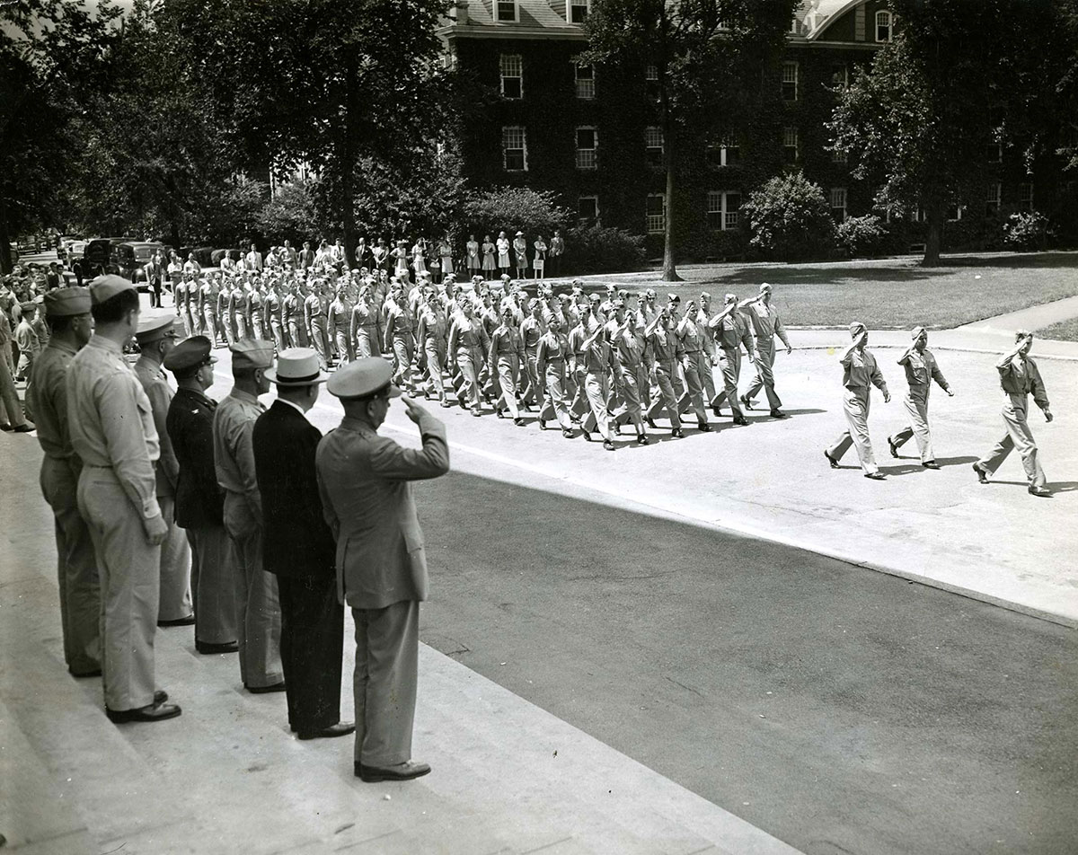 ROTC soldiers marching through HBS campus with officers standing on the steps of Baker Library.