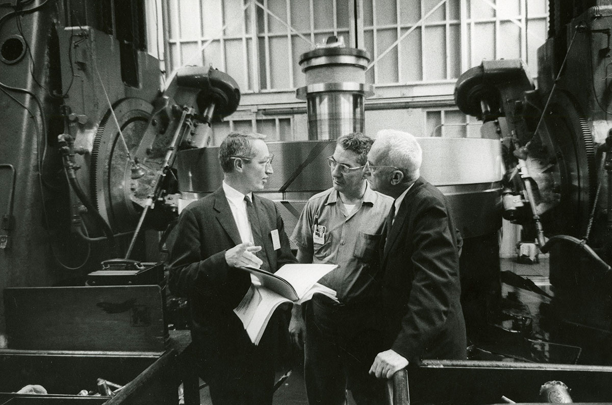 HBS Professor Paul R. Lawrence speaking to two businessmen in a factory.