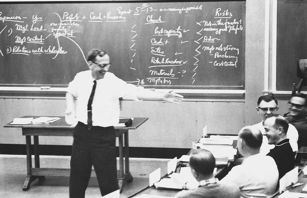 Black and white photograph of HBS Professor Clayton Christensen gesturing toward a student while teaching.
