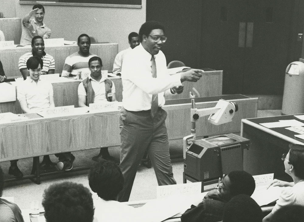 Black and white photograph of Professor James I. Cash teaching in classroom, surrounded by students.